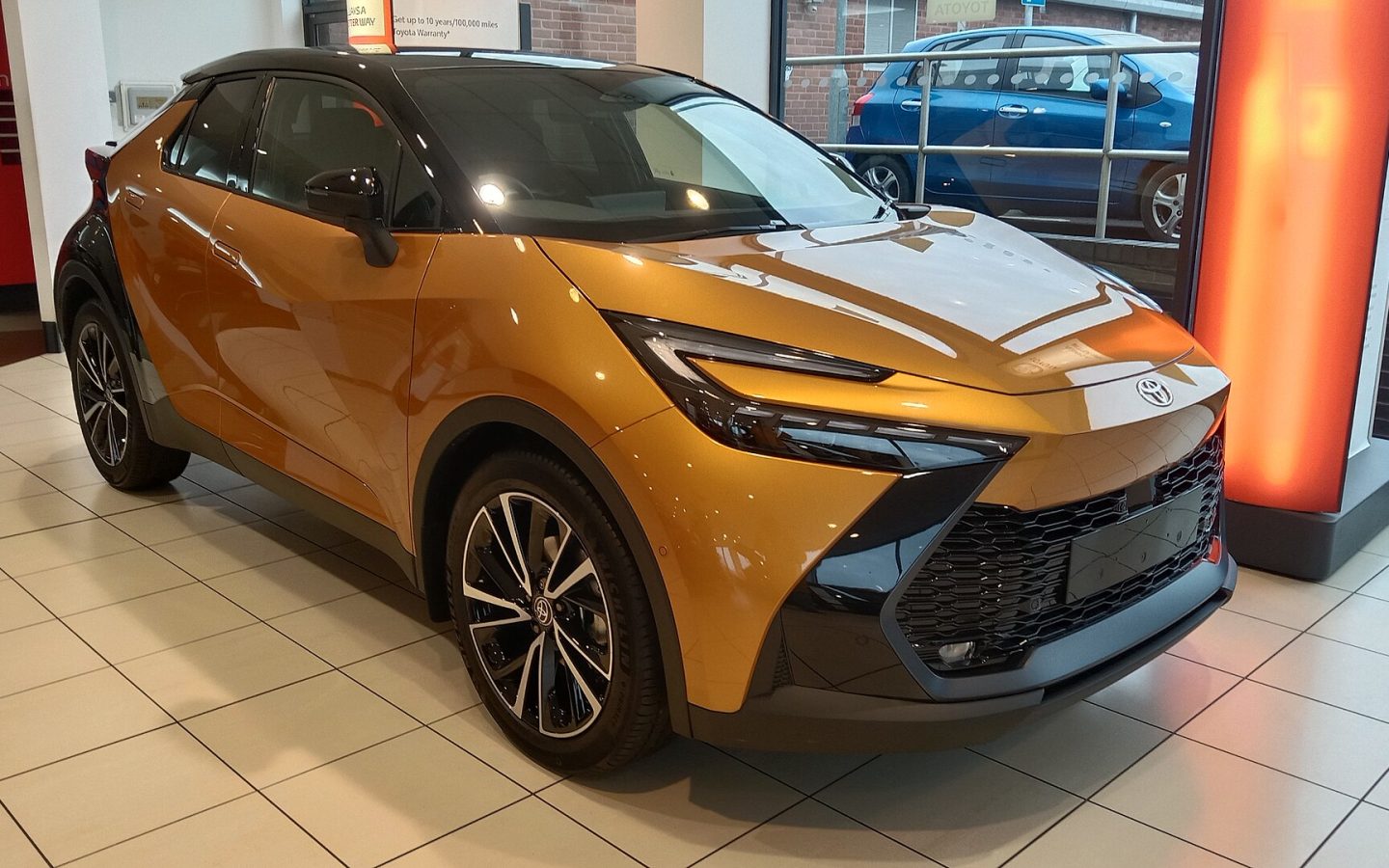 Toyota C-HR de deuxième génération jaune à toit noir, vue avant trois quarts en showroom ; illustration européenne non contractuelle