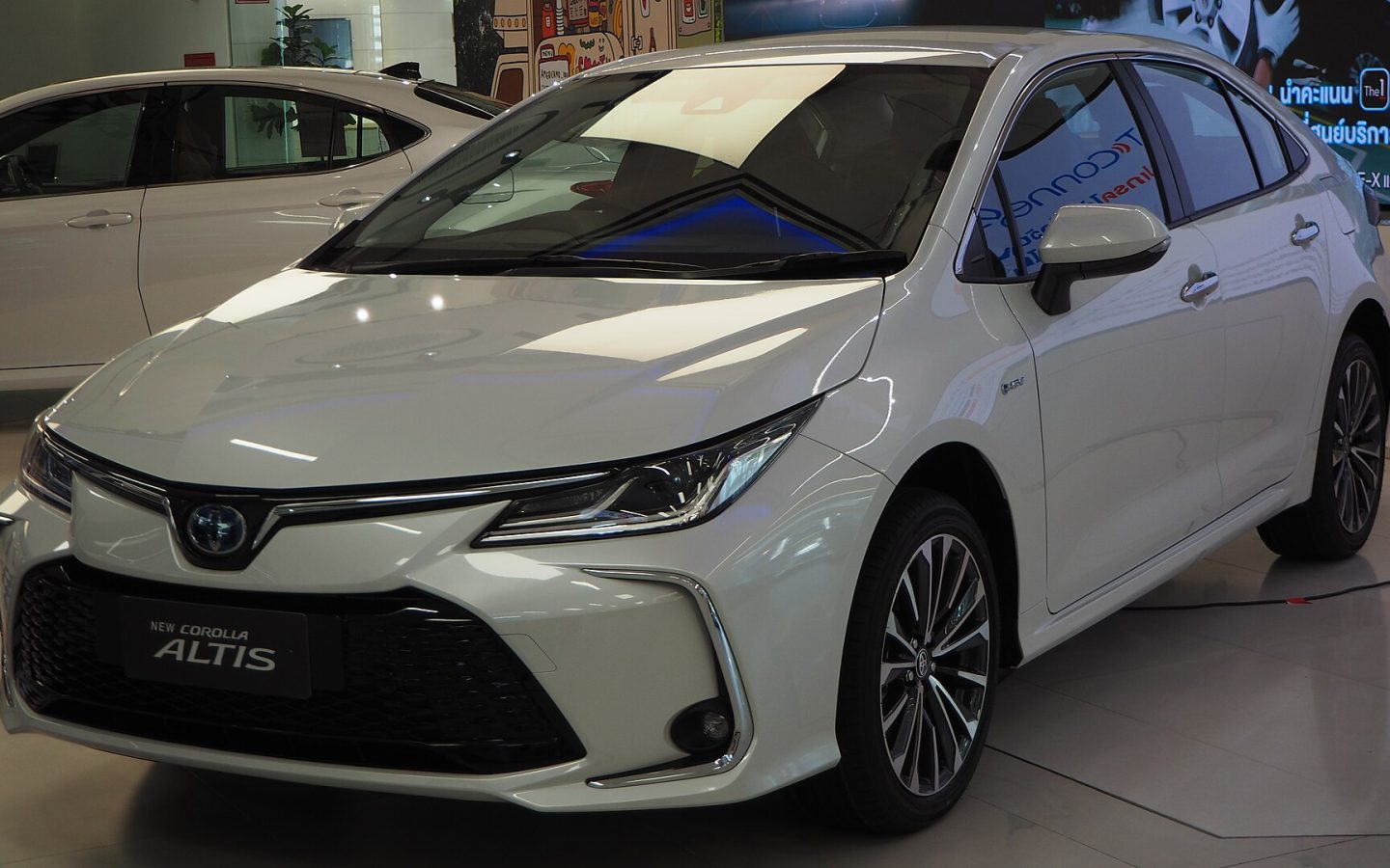 Toyota Corolla berline restylée blanche, vue de trois quarts avant en showroom ; illustration thaïlandaise non contractuelle
